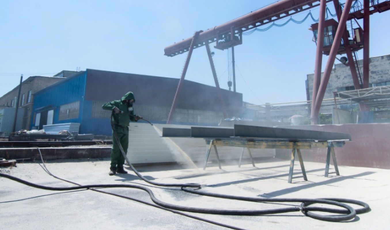 Operator in protective clothing blasting a steel structure
